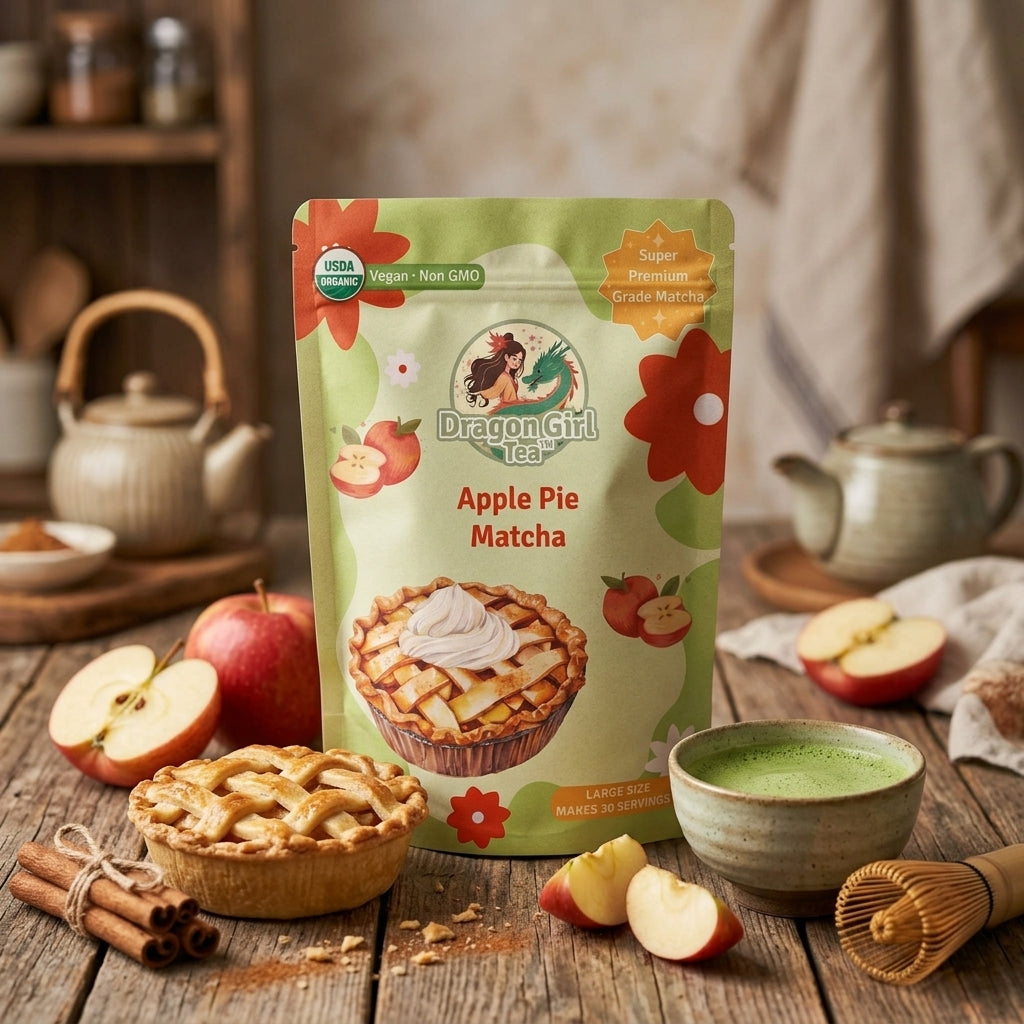 A stand-up pouch of Dragon Girl Tea Apple Pie Matcha is displayed on a rustic wooden table with an apple pie, sliced apples, a bowl of green tea, cinnamon sticks, and teaware in the background.